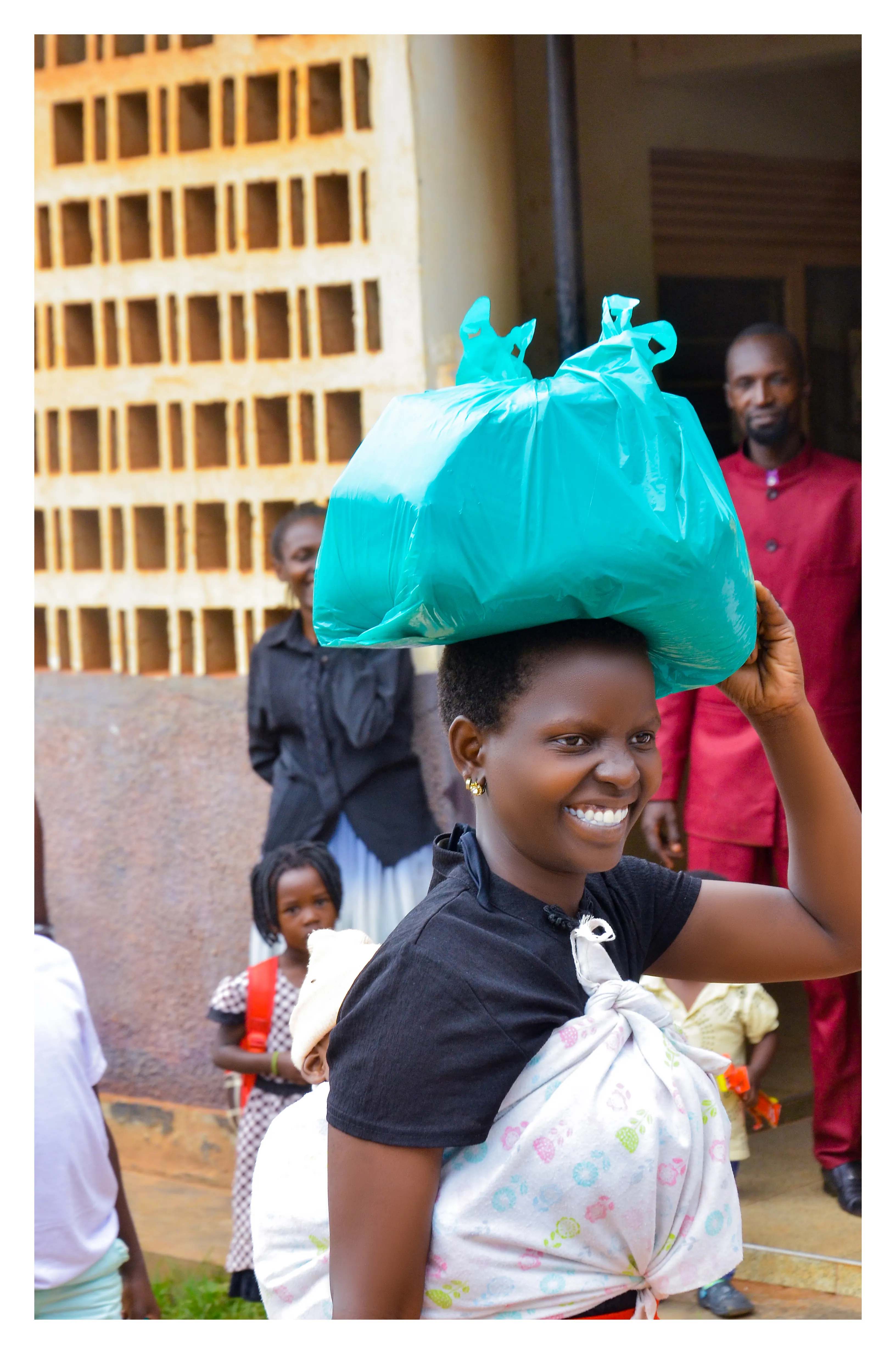 A young Ugandan mother smiling with a package of essential supplies